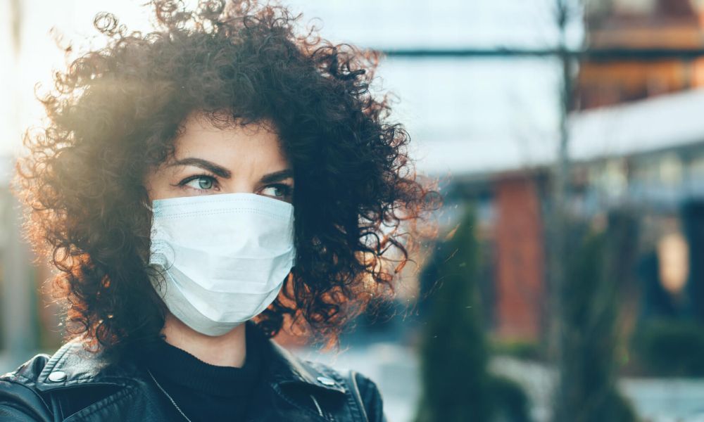Curly haired caucasian woman wearing an covid mask while posing outside on front of a building
