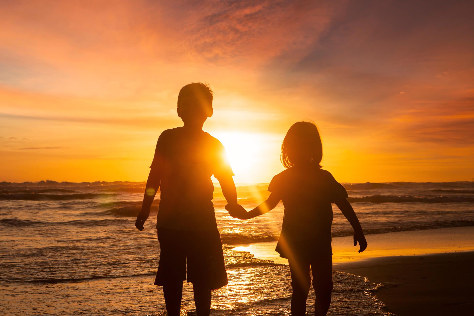 two kids on a beach with their guardian at sunset
